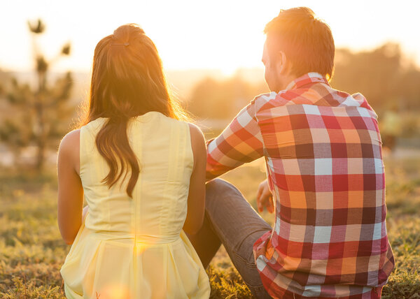 Back view of young happy couple sitting on river.