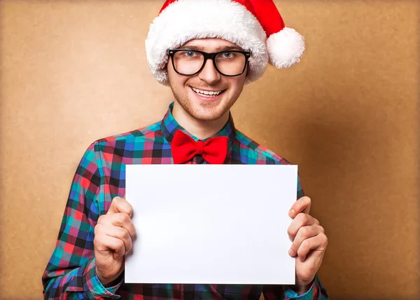 Hipster guy i hatten jultomten innehar ett ark papper. — Stockfoto