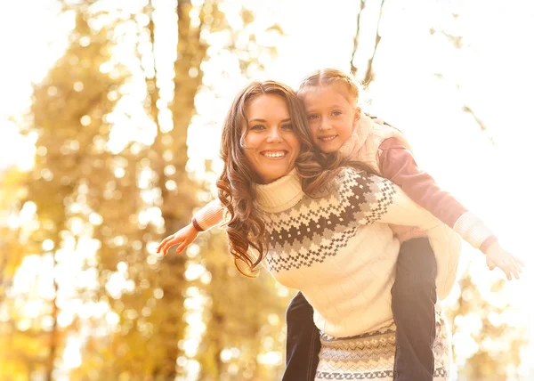 Mor ger dotter piggyback rida i höst skog — Stockfoto