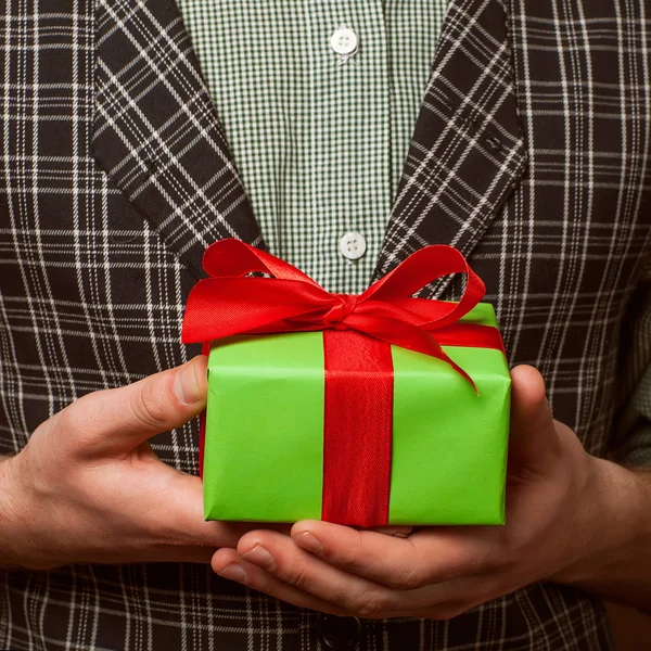 Tipo sosteniendo un regalo en un traje y pajarita en una jaula — Foto de Stock