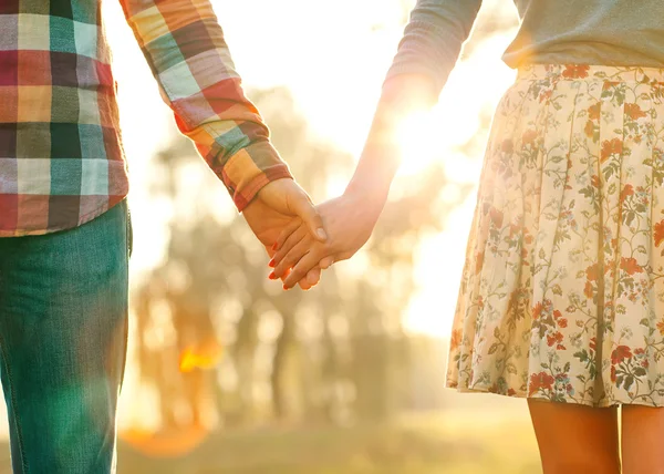 Молодая пара влюбленных гуляет по осеннему парку, держась за руки — стоковое фото