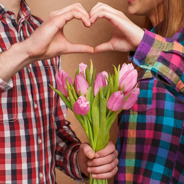 Jovem casal apaixonado fazer um coração e as mãos estão segurando um buquê de tulipas — Fotografia de Stock