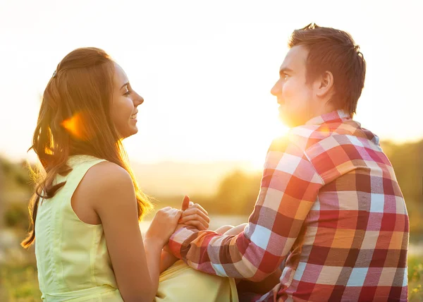 Visão traseira do jovem casal feliz sentado no rio ao pôr do sol — Fotografia de Stock