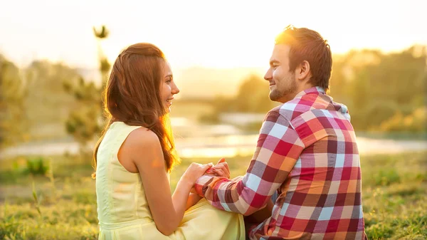 Visão traseira do jovem casal feliz sentado no rio ao pôr do sol — Fotografia de Stock