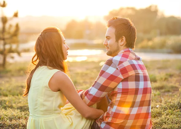 Vista trasera de la joven pareja feliz sentada en el río al atardecer — Foto de Stock