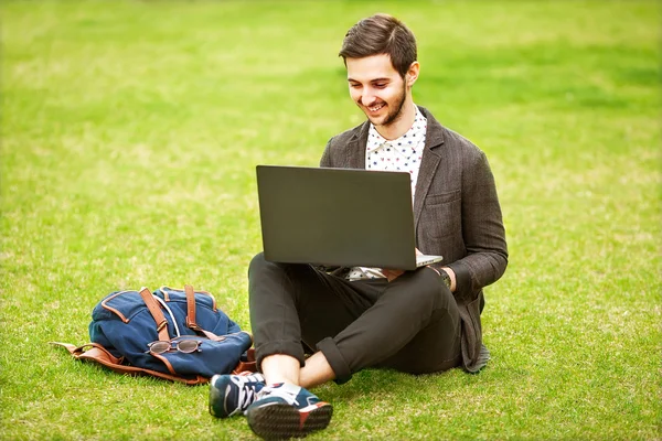 Joven estudiante masculino de moda sentado en el césped en el parque —  Fotos de Stock