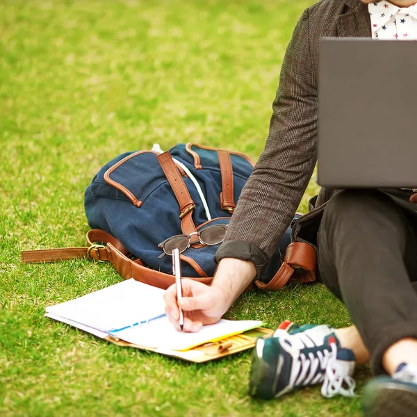 Jonge mode mannelijke student zittend op het gras in park en bedrijf — Stockfoto