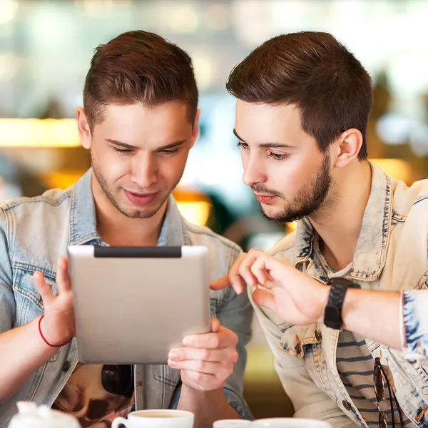 Two young students using tablet computer in cafe — Stock Photo, Image