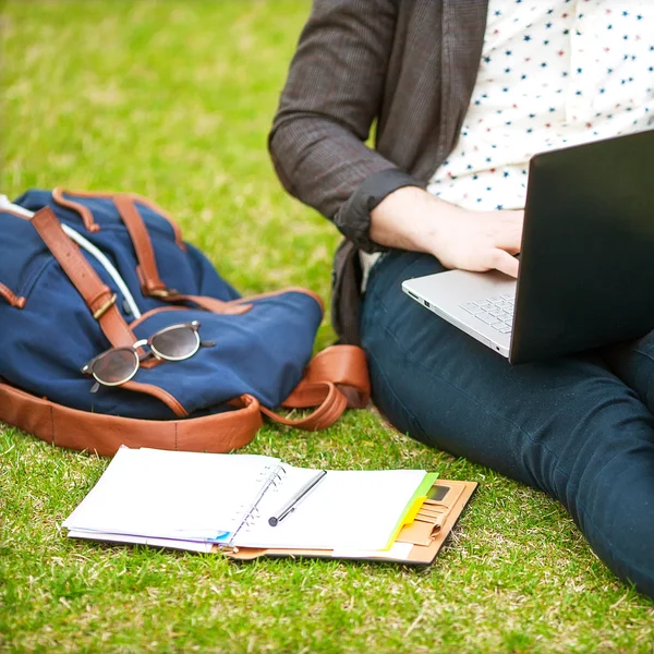Jonge man met zijn laptop op het gras en maakt notities in een niet — Stockfoto