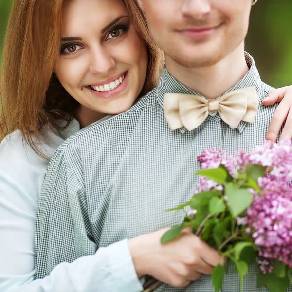 Casal apaixonado no parque sorrindo segurando um buquê de flor lilás — Fotografia de Stock