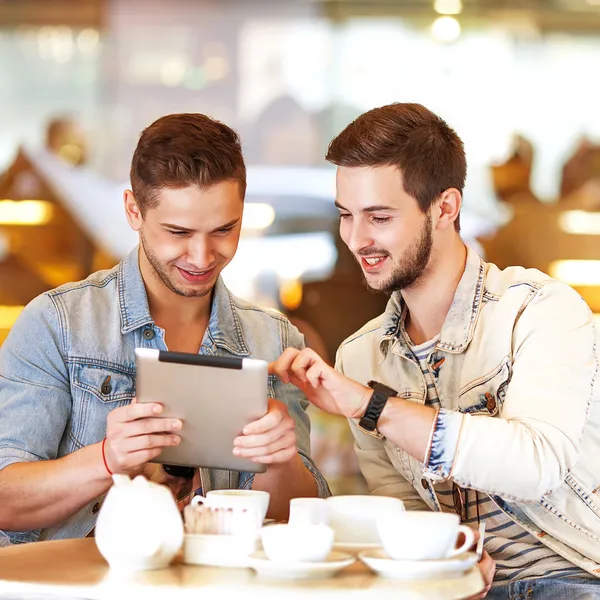 Two young students using tablet computer in cafe — Stock Photo, Image