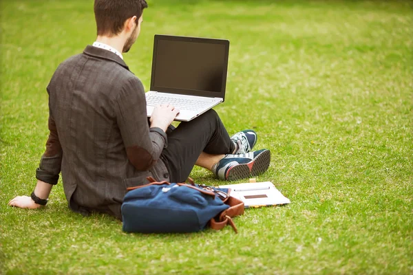 Joven estudiante masculino de moda sentado en el césped en el parque — Foto de Stock