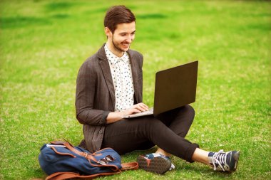 young fashion male student sitting on grass in park and holding  clipart
