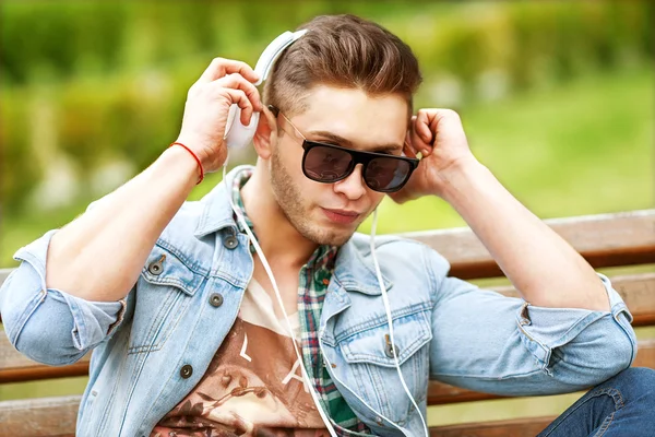 Bonito moda homem ouvindo música na grama no parque — Fotografia de Stock