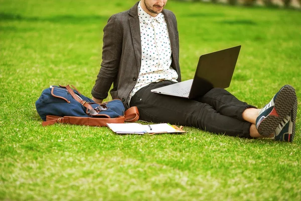 Jonge mode mannelijke student zittend op het gras in park en bedrijf — Stockfoto