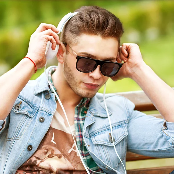 Bell'uomo di moda che ascolta musica sull'erba nel parco — Foto Stock