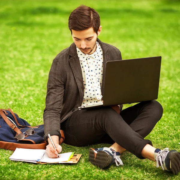 Joven estudiante masculino de moda sentado en el césped en el parque —  Fotos de Stock