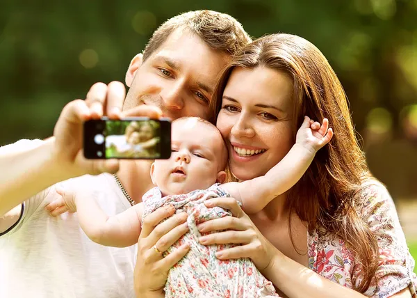 携帯電話で selfie を取って公園で赤ちゃん連れのご家族 — ストック写真