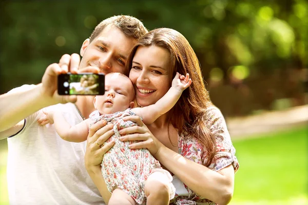 Familia con bebé en el parque tomando selfie por teléfono móvil —  Fotos de Stock