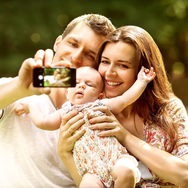 携帯電話で selfie を取って公園で赤ちゃん連れのご家族 — ストック写真