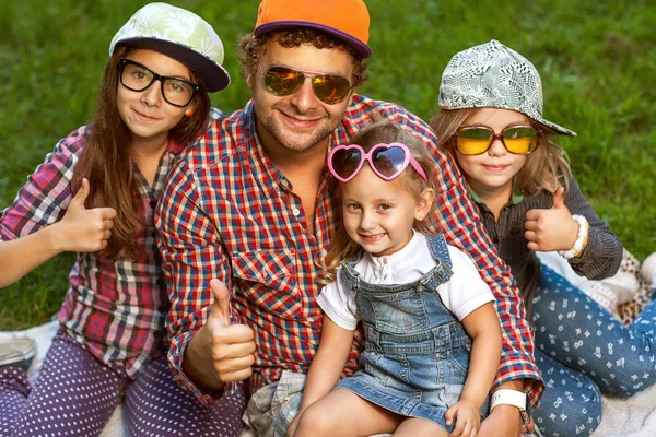 Vader en zijn 3 dochters liggen op het gras in zonnebril gelukkig. — Stockfoto