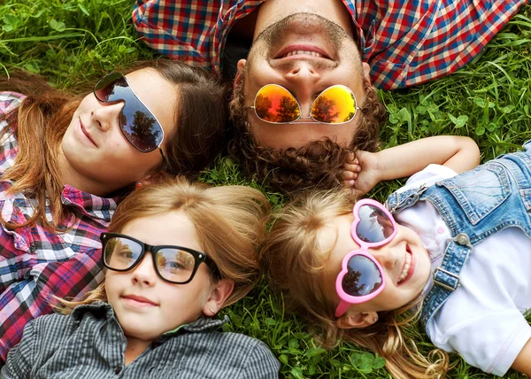 Dad and his 3 daughters lie on the grass in sunglasses happy hip — Stock Photo, Image