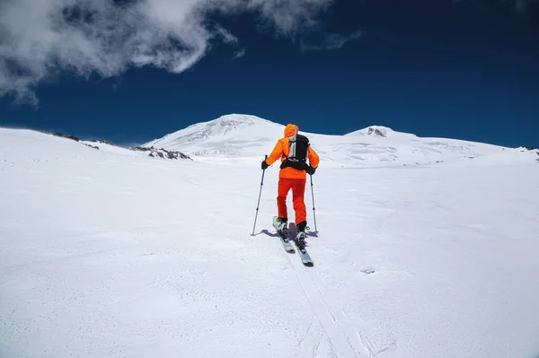 Ein junger Sportler im orangefarbenen Anzug erklimmt eine Skitour auf einem schneebedeckten Hang zum Elbrus. Kopierraum. Winterbergsteigen — Stockfoto