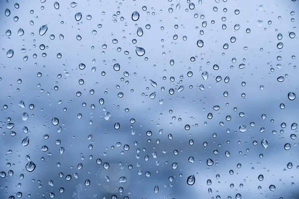 Капли воды на стекле в дождливую погоду с небольшими спальными районами на заднем плане. Осенний холодный влажный фон — стоковое фото