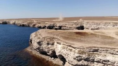 Tozlu bir şeytan, kumlu bir kıyıdaki bir kasırga kuru bir çalılığın içinden şiddetle geçer. Bozkır manzaralı tozlu arazi turistleri. Doğal fenomen