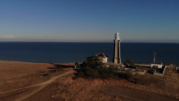 Aerial view of a lonely lighthouse surrounded by technical buildings stands on a deserted rocky promontory on the seashore. Oceanic evening shore. Lighthouse at sunset. Low key. film grain — Stock Video