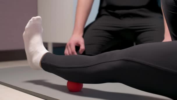 Närbild Ung manlig massageterapeut lär klient Kaukasiska kvinna patient myofascial själv massage av ben och höfter med hjälp av massage boll inomhus. Myofaskulär frisättning — Stockvideo