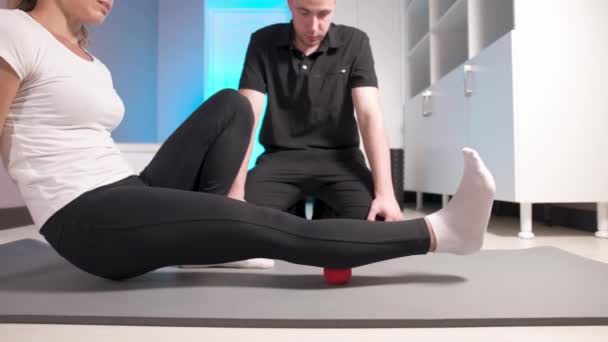 Egy fiatal férfi masszázsterapeuta egy kliens fehérbőrű nő myofascial ön-masszázsát tanít egy masszázsgolyóval. Myofascealis felszabadulás — Stock videók