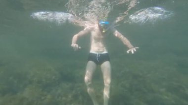 Sıska sakallı, maske takmış, su altında dinlenen beyaz bir adam. El sallıyor ve kabarcıklar yaratıyor