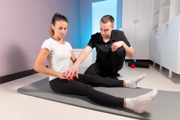 Eliberare miofascială. Un fizioterapeut de sex masculin plasează o minge pentru reabilitarea mușchilor picioarelor clienților în timp ce se așează tehnica folosind o minge roșie. Conceptul de automasaj. Utilizare practică. — Fotografie, imagine de stoc