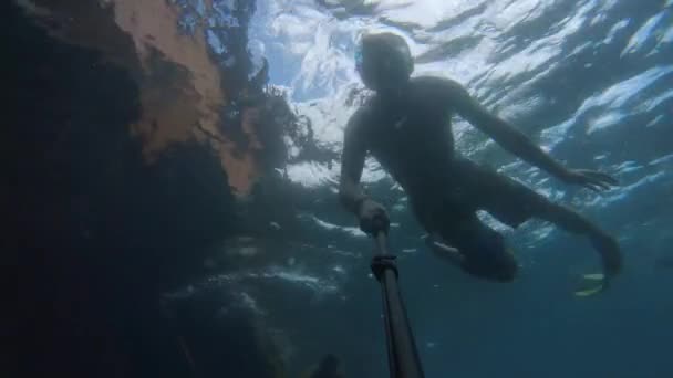 Il giovane in maschera nuota sott'acqua accanto a una barca affondata. Selfie stick action camera — Video Stock