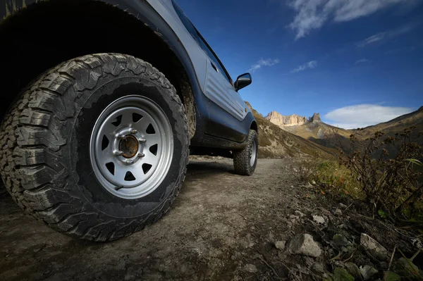 Une grande roue de SUV avec une grande bande de roulement de boue se dresse sur une route rocheuse dans le contexte des montagnes. Voyage en véhicules tout-terrain. Tourisme auto-guidé en voiture privée. — Photo