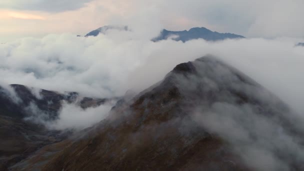 Close movement flies along endless mountains through the clouds. An aerial view of a landscape of clouds floats halfway along a mountain range at dusk. Mountain weather, epic climate change — Stock Video