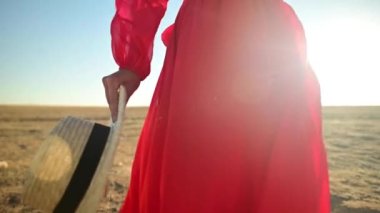 Kuru çimenlerde yürüyen bir kadının sinematik yavaş çekimi. Sandaletlerle kumlu bozkırın dalgalı yüzeyinde rüzgarda sallanan elbiseli bir kadın gezgin.