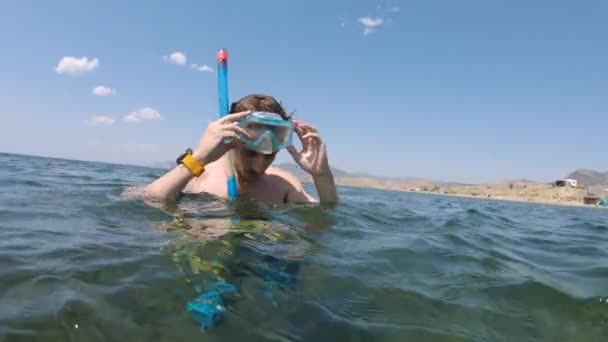 ダイビングの準備をしている白人の若者は水中に立っている間にシュノーケリングマスクを準備します. — ストック動画