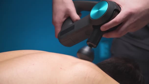Caucasian professional male masseur makes a healing effect on the muscles of the upper back of a male client using a percussion vibro massager. Shock therapy for regenerating massage athletic body. — Stock Video