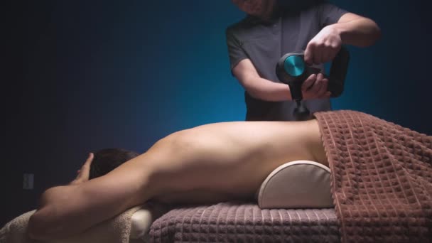 Masseur masculin professionnel caucasien faisant des exercices de massage pour le bas du dos et le muscle carré du dos à un client masculin à l'aide d'un vibromasseur à percussion. Thérapie de choc pour régénérer le massage — Video