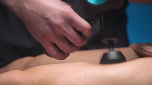 Mužský masér provádějící masážní cvičení na stehnech s pomocí perkusního vibračního masážního zařízení pro mužského klienta. Šoková terapie pro regenerační masáž sportovního těla. — Stock video
