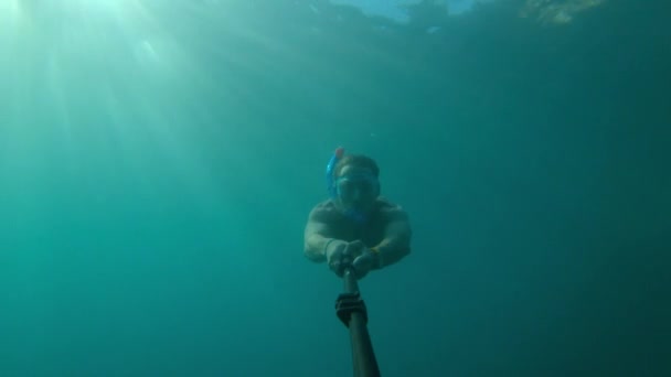 Jeune homme caucasien nageant sous l'eau en apnée sous masque et tuba avec des nageoires prenant des photos de lui-même sur selfie stick et caméra d'action — Video