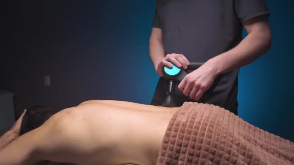 Massage par ondes de choc à percussion avec un masseur électrique. Massez le bas du dos d'un athlète masculin dans une salle de massage professionnelle — Video