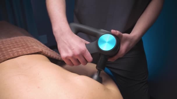 Percussion shock wave massage using an electric massager. Massage the lower back of a male athlete in a professional massage room — Stockvideo