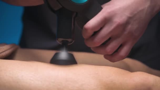 Close-up Man male masseur massages the leg of a male athlete client with a massage percussion apparatus. Shock wave therapy — Stockvideo