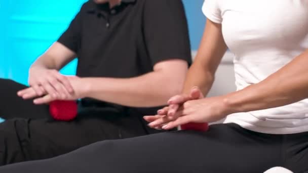 Közelkép Myofascial kiadás. Egy férfi fizioterapeuta elhelyezi a labdát a rehabilitáció az ügyfelek láb izmok, miközben ül technika segítségével egy piros labdát. Önmasszázs koncepció. Gyakorlati alkalmazás. — Stock videók