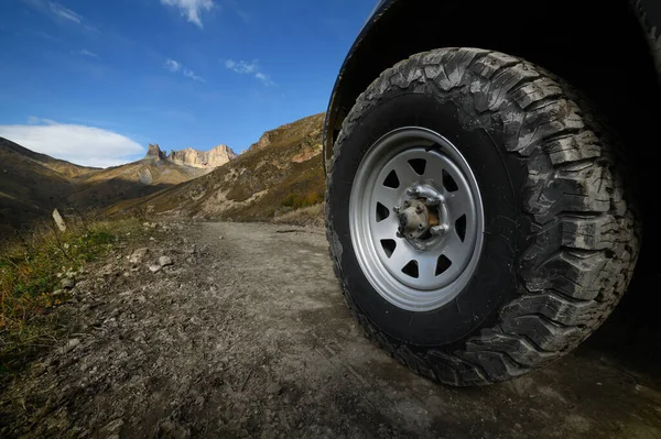 Décryptages Une grande roue tout-terrain hors route se dresse sur une route accidentée dans les montagnes, sur fond de rochers. Excursions hors route et concept de voyage hors route — Photo