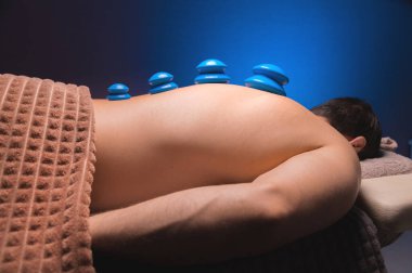 Çıplak bir adamın sırtında kupa terapisi için elektrikli süpürge bardakları. Spa 'da masaj, sırtın için tıbbi tedavi. Canlandırıcı ve rahatlatıcı masaj, fitness tedavileri