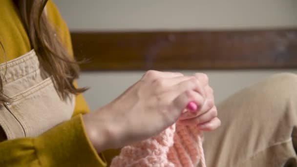 Close-up. Hands of an attractive young caucasian woman in casual clothes sitting on a sofa indoors knits a woolen product by a crochet — Stock Video